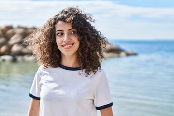 Young hispanic woman smiling confident looking to the side at seaside