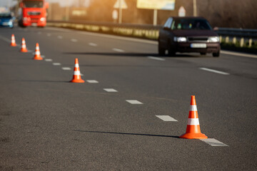A row of traffic orange striped cones on the road. sunlight. These objects are temporary traffic control devices for directing and avoiding sections of the road being repaired or diverting traffic.