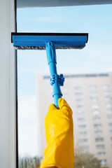 Man in yellow gloves cleaning window with squeegee and spray detergent at home terrace. House...
