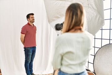 Woman photographer talking pictures of man posing as model at photography studio looking away to side with smile on face, natural expression. laughing confident.