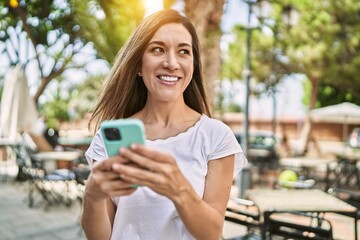 Young hispanic woman smiling confident using smartphone at park