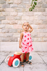 Fototapeta premium Little girl stands and looks up near a toy car. High quality photo