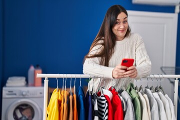 Young brunette woman waiting for laundry using smartphone smiling looking to the side and staring away thinking.