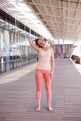 Beautiful strong muscular woman doing stretching on mat on terrace outdoors. Healthy young adult girl in sportswear stretch alone. Fit thin gimnast doing yoga and pilates, training on mat. Perspective