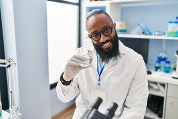 Young african american man wearing scientist uniform holding diamond at laboratory