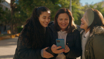 Mother and daugthers using smartphone standing together at park