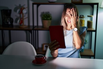 Young hispanic woman using touchpad sitting on the table at night yawning tired covering half face, eye and mouth with hand. face hurts in pain.