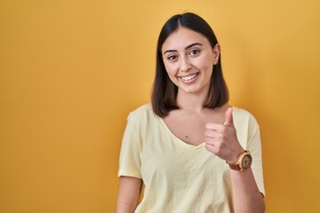 Hispanic girl wearing casual t shirt over yellow background doing happy thumbs up gesture with hand. approving expression looking at the camera showing success.