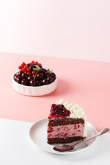 A piece of biscuit cake, with cherry souffle with cream cheese and cherry confiture on a pink and white background. Vertical photo