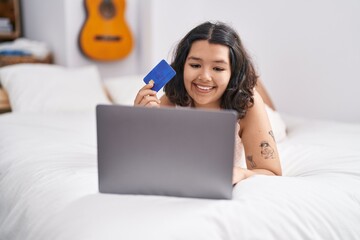 Young woman using laptop and credit card lying on bed at bedroom