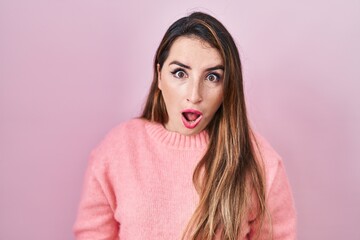 Fototapeta premium Young hispanic woman standing over pink background in shock face, looking skeptical and sarcastic, surprised with open mouth