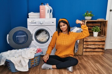 Young hispanic woman doing laundry strong person showing arm muscle, confident and proud of power