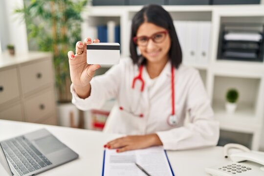 Young latin woman wearing doctor uniform holding credit card at clinic