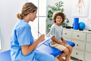 Obraz premium Mother and son wearing physiotherapist uniform having rehab session writing on clipboard at physiotherapy clinic