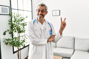 Middle age hispanic man wearing doctor uniform and stethoscope at waiting room smiling with happy...