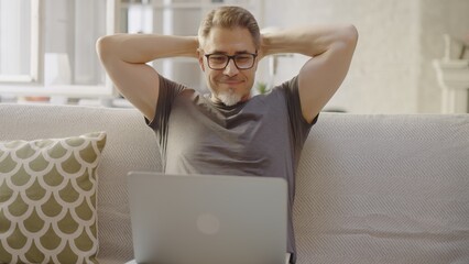 Older man working online with laptop computer at home sitting on couch in living room. Home office,...