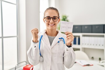 Young doctor woman holding covid certificate screaming proud, celebrating victory and success very excited with raised arms