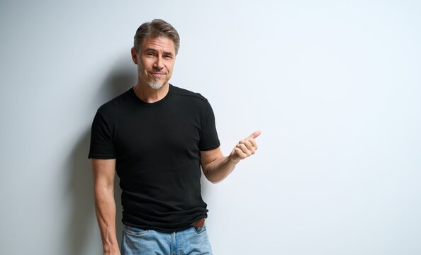 Portrait Of Happy Casual Older Man Smiling, Showing, Pointing At Invisible Product Or Text, Asking. Mid Adult, Mature Age Guy At White Wall, Isolated On White Background, Copy Space.