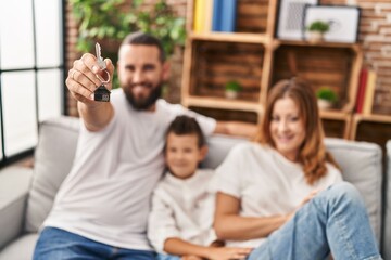 Family holding key of new house hugging each other sitting on sofa at home