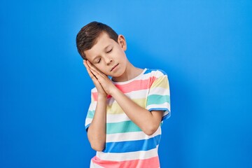 Fototapeta na wymiar Young caucasian kid standing over blue background sleeping tired dreaming and posing with hands together while smiling with closed eyes.