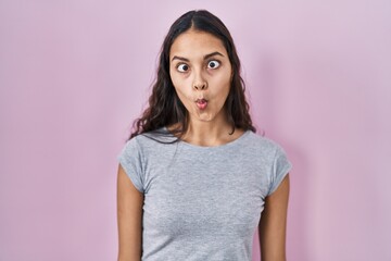 Obraz premium Young brazilian woman wearing casual t shirt over pink background making fish face with lips, crazy and comical gesture. funny expression.