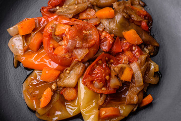 Baked vegetables, eggplant, peppers and carrots on a black plate on concrete background
