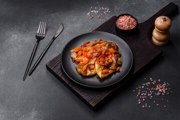 Baked vegetables, eggplant, peppers and carrots on a black plate on concrete background