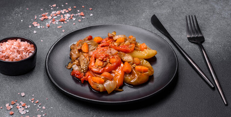 Baked vegetables, eggplant, peppers and carrots on a black plate on concrete background