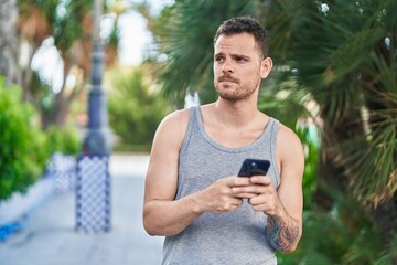 Young hispanic man using smartphone with serious expression at park