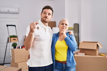 Hispanic mother and son holding keys of new home serious face thinking about question with hand on...