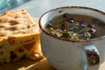 sweet cake with raisins and dried apricots, mug with herbal tea on a wooden board, natural light from the window. Horizontal photo