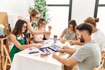Group of young paint students smiling happy and drawing sitting on the table at art studio.