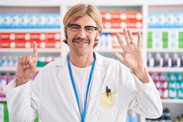 Caucasian man with mustache working at pharmacy drugstore showing and pointing up with fingers number six while smiling confident and happy.
