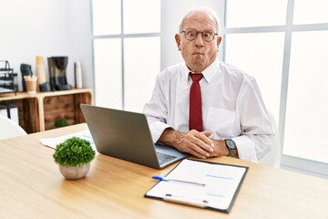 Senior man working at the office using computer laptop making fish face with lips, crazy and comical gesture. funny expression.