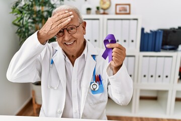 Senior doctor man holding purple ribbon awareness stressed and frustrated with hand on head, surprised and angry face
