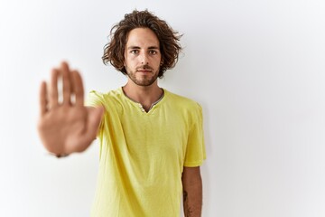 Young hispanic man standing over isolated background doing stop sing with palm of the hand. warning expression with negative and serious gesture on the face.