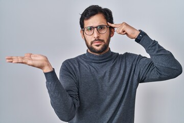 Handsome latin man standing over isolated background confused and annoyed with open palm showing...
