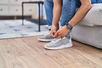Young hispanic man tying shoe at home