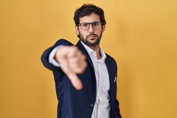Handsome latin man standing over yellow background looking unhappy and angry showing rejection and negative with thumbs down gesture. bad expression. - obrazy, fototapety, plakaty