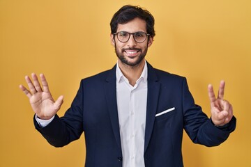 Handsome latin man standing over yellow background showing and pointing up with fingers number seven while smiling confident and happy.