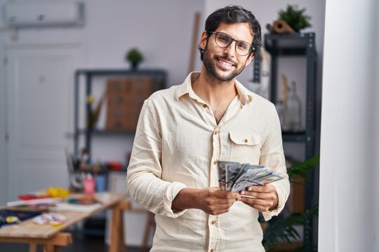 Young hispanic man artist smiling confident counting dollars at art studio