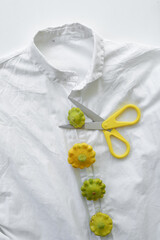 scissors with a yellow handle lie on a shirt and cut a button from a fresh vegetable. original style