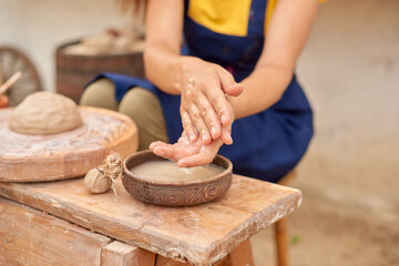 female craftsman wets her hands in a bowl of water to form clay