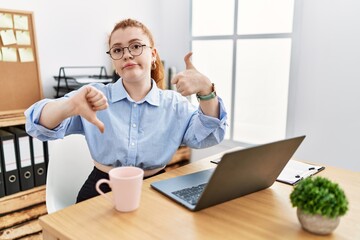 Young redhead woman working at the office using computer laptop doing thumbs up and down, disagreement and agreement expression. crazy conflict
