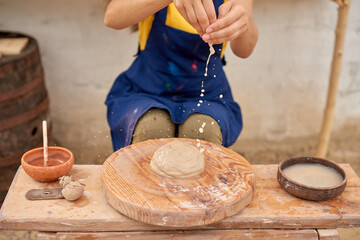 female craftsman wets her hands in a bowl of water to form clay