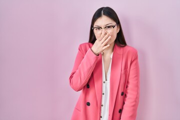 Chinese business young woman wearing glasses smelling something stinky and disgusting, intolerable smell, holding breath with fingers on nose. bad smell