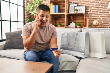 Obraz premium Hispanic young man doing payment with credit card on the phone smiling and laughing hard out loud because funny crazy joke.