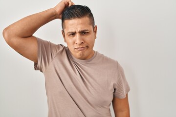 Hispanic young man standing over white background confuse and wonder about question. uncertain with doubt, thinking with hand on head. pensive concept.