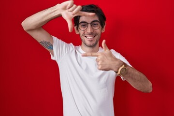 Young hispanic man standing over red background smiling making frame with hands and fingers with happy face. creativity and photography concept. © Krakenimages.com