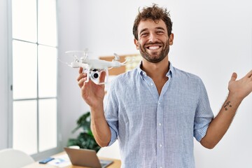 Young handsome man using drone at architect office celebrating achievement with happy smile and winner expression with raised hand